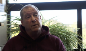 Screenshot of Injured worker Wayne in red sweatshirt from linked video